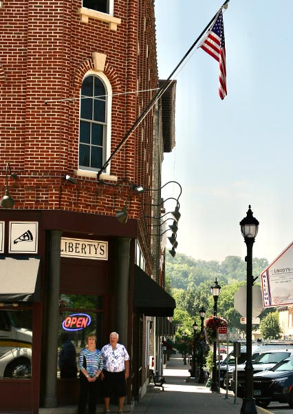 Two people stand outside Libertys Bar café in a brick building with an American flag above.