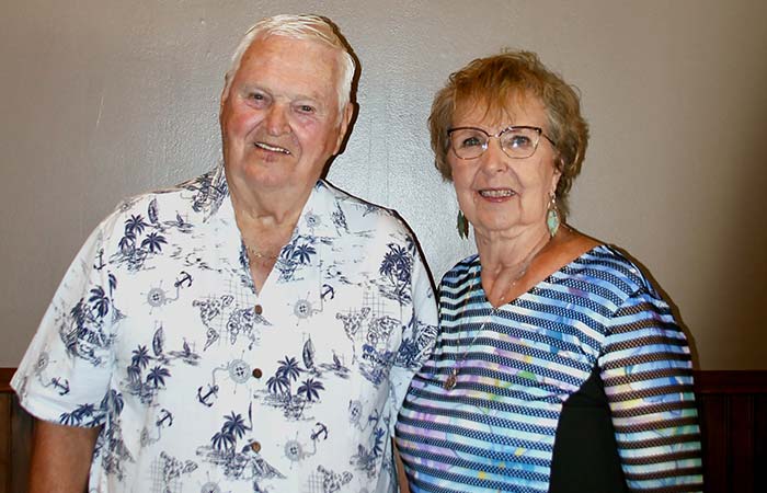 Smiling older man in a palm tree shirt stands beside a smiling woman at a Minnesota restaurant.