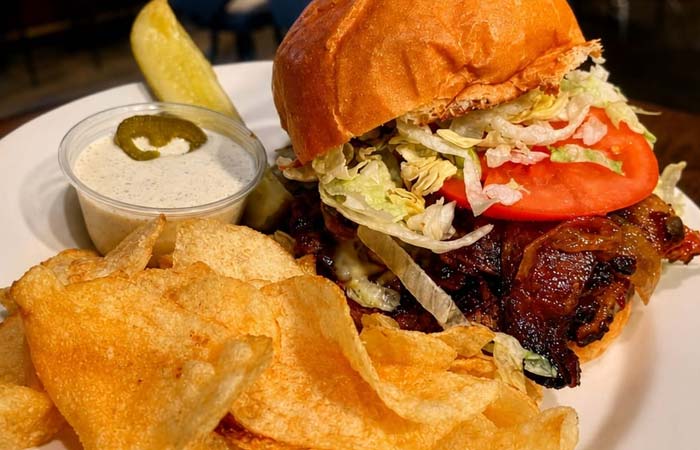 Burger with lettuce, tomato, and bacon at our downtown bar, served with chips, dip, and a pickle.