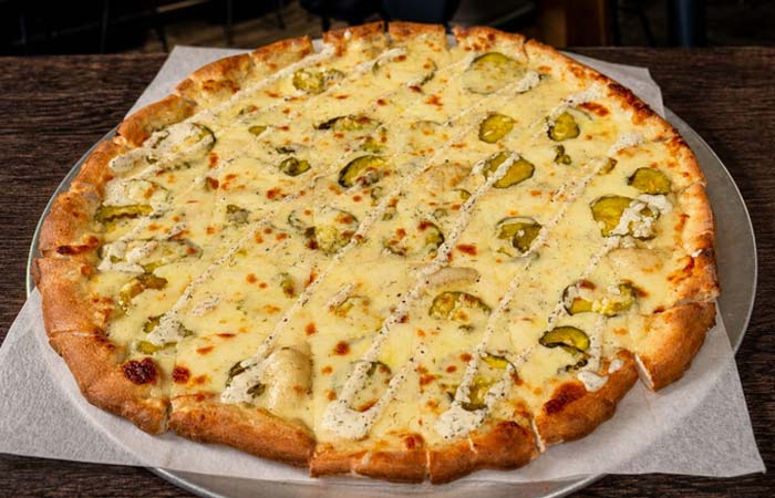 A cheese pizza from Liberty’s Bar, topped with pickles, cut in strips on a metal tray.