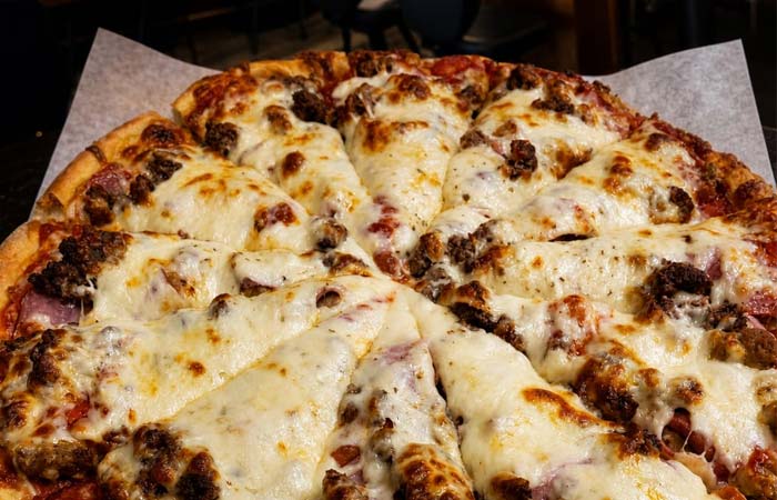 A close-up of a cheesy, sliced meat pizza at Libertys in Downtown Red Wing MN on parchment paper.