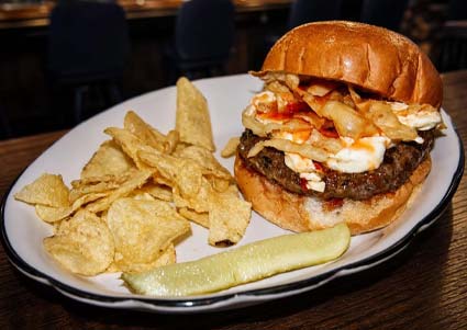 Libertys burger with chips, topped with onions and sauce, served in Red Wing MN on a white plate.